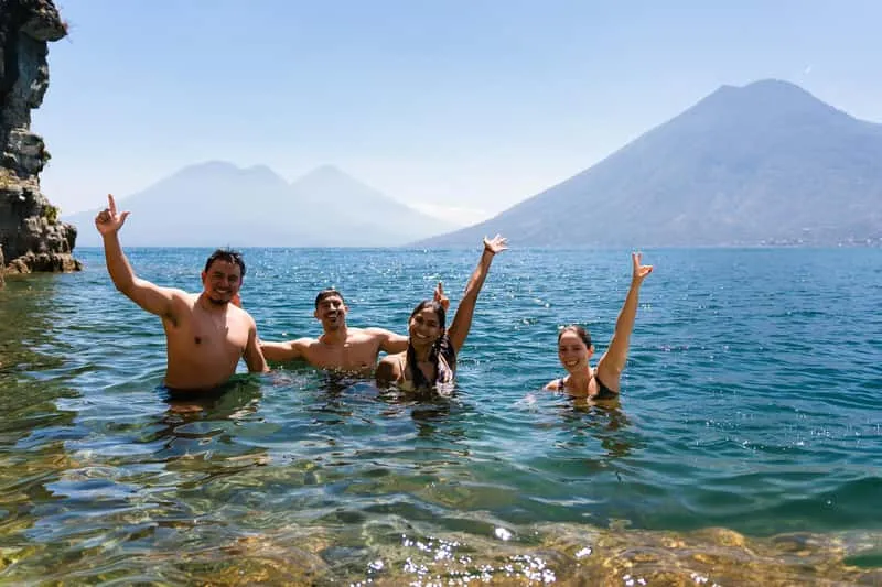 Traveler jumping from the 12-meter cliff platform at Tzankujil Nature Reserve on Lake Atitlán with volcanic panorama behind, adventure boat tour